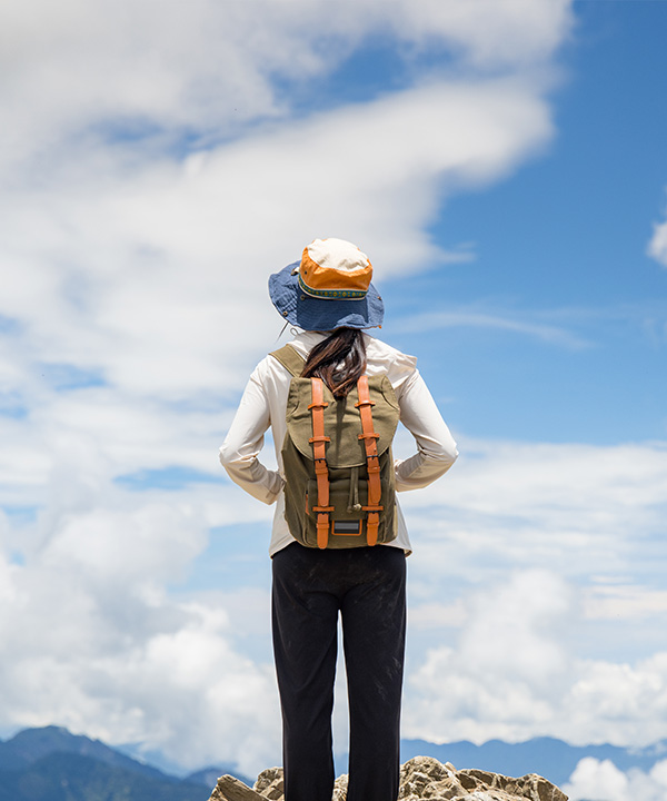 A woman standing on top of a mountain looking at clouds.